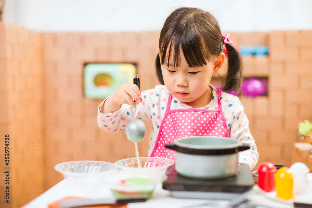 toddler girl pretend play food preparing role against cardboard blocks kitchen background toddler girl pretend play food preparing role against cardboard blocks kitchen background
