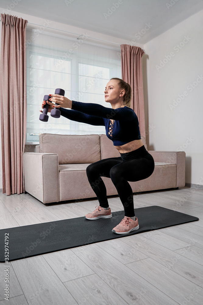 Sporting a beautiful young girl performs exercise with dumbbells at home.