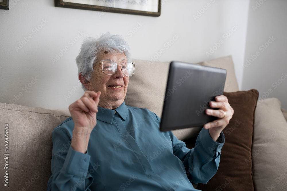 Smiling happy senior Caucasian woman sitting in her living room and making a video call on a tablet Smiling happy senior Caucasian woman sitting in her living room and making a video call on a tablet