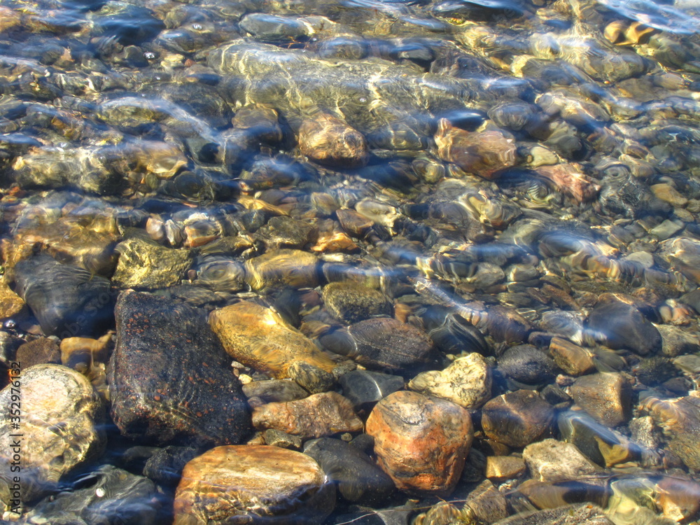 Sea ​​stones under water with glare of the sun on the surface 