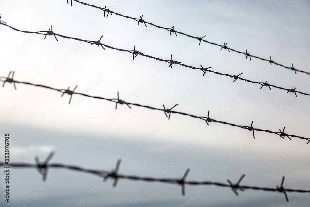 Barbed wire in several rows against the sky. Close-up. Horizontal orientation. Barbed wire in several rows against the sky. Close-up. Horizontal orientation.