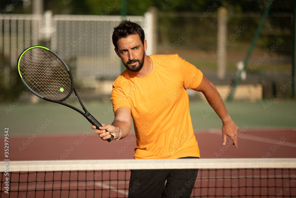 a concentrated and smiling tennis player volleying a tennis ball on an outdoor tennis court