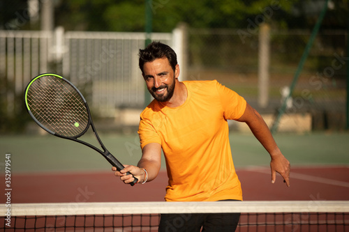 a concentrated and smiling tennis player volleying a tennis ball on an outdoor tennis court © kevin