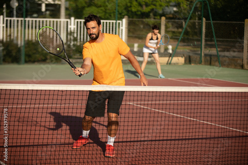 a concentrated and smiling tennis player volleying a tennis ball on an outdoor tennis court