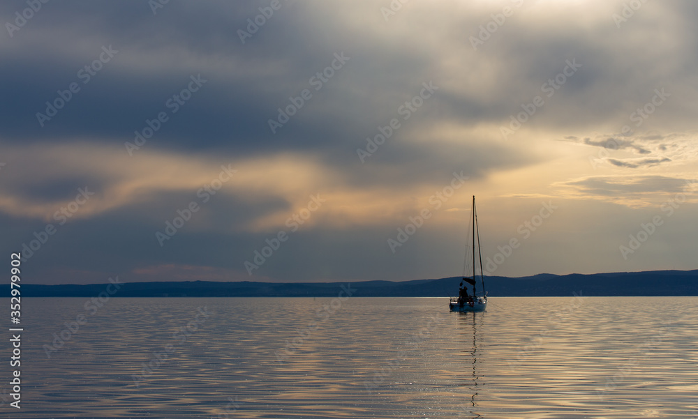 Sailing boat on lake Balaton with dramatic clouds and hills in the background at sunset. Rule of thirds landscape with space for text