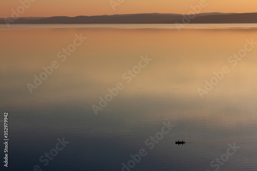 Small fishing boat on peaceful and lake Balaton at sunset with gradient colors and mountains in the background