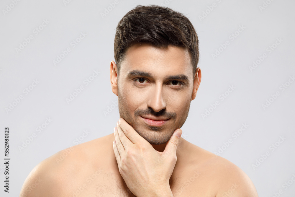 Handsome shirtless guy looking at camera, touching chin with fingers, feeling calm and confident, concept of skin care, isolated on gray background Handsome shirtless guy looking at camera, touching chin with fingers, feeling calm and confident, concept of skin care, isolated on gray background