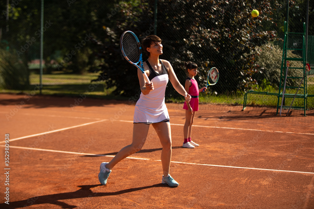 a mother and daughter playing tennis outdoors and having fun