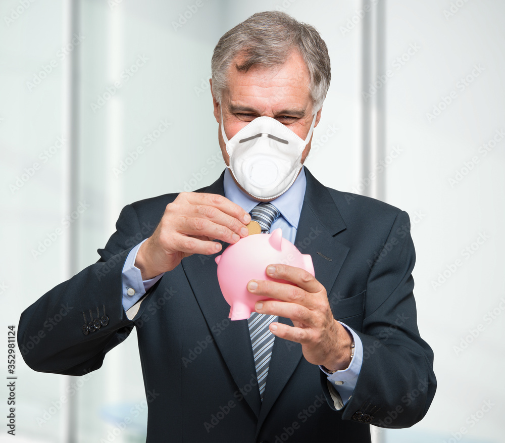 Masked businessman putting money in a piggy bank Masked businessman putting money in a piggy bank