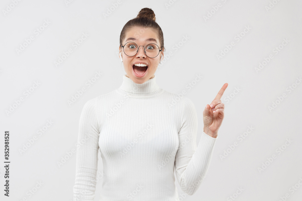 Young female feeling excited and shocked with great commercial offer, pointing to right side of photo, isolated on gray background Young female feeling excited and shocked with great commercial offer, pointing to right side of photo, isolated on gray background