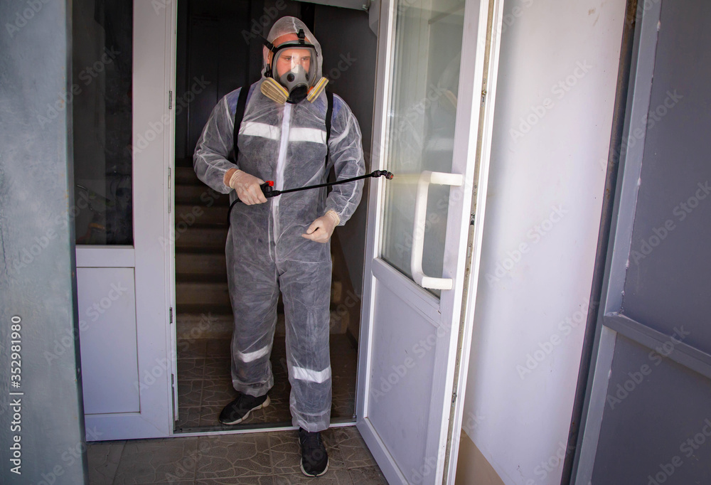 A man in a disposable suit for disinfection, his face is covered with a reusable mask with filters, and his hands are wearing latex medical gloves. Disinfects public premises, entrances, elevators fro A man in a disposable suit for disinfection, his face is covered with a reusable mask with filters, and his hands are wearing latex medical gloves. Disinfects public premises, entrances, elevators fro