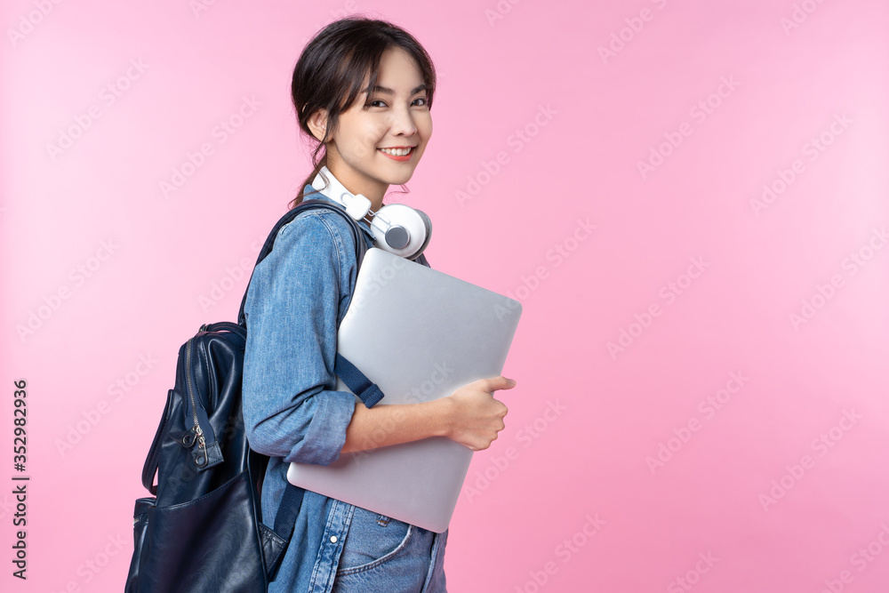 Portrait of smiling young Asian college student with laptop and backpack isolated over pink background - obrazy, fototapety, plakaty 