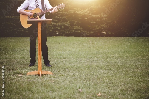 Картината върху платно Young male in a park holding a guitar and playing a song from the Christian hymn