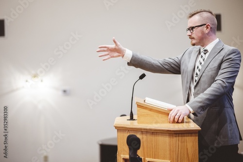 Male in a formal outfit preaching the Holy Bible from the tribune at the altar o Fototapet