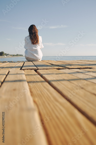 Woman sitting at the harbour on the quay with her back to the camera looking to sea. long dark hair