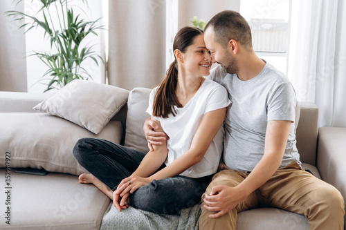 Photography Beautiful couple in love in stylish casual wear hugging while sitting on a sofa at home