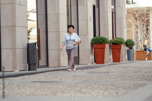 Aged woman wearing casual clothes while walking on the street.