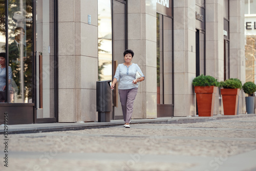 Aged woman wearing casual clothes while walking on the street. © lialia699