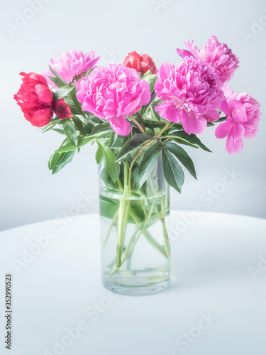 glass vase on the white table with pink peons in close up view