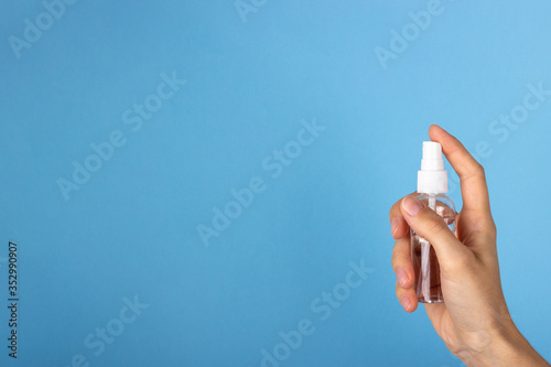 A young woman holds the antiseptic in her hand. The bottle of sanitizer in the girl's hand on a blue background. Health care concept
