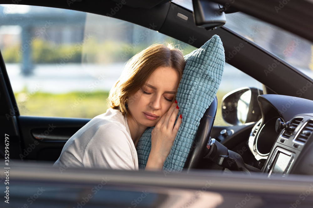 Tired young woman driver asleep on pillow on steering wheel, resting after  long hours driving a car. Fatigue. Sleep deprivation. Stock Photo