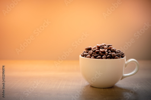 Roasted coffee beans in a white coffee mug placed on a wooden table and have space to put text.