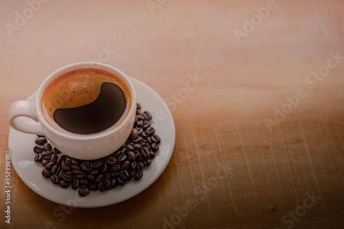 Rich coffee with a soft creamy foam in a white coffee cup with coffee beans on the plate. Try the glass on a wooden table with space to put text.