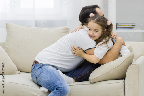 Father and daughter sitting on white sofa and hugging each other.