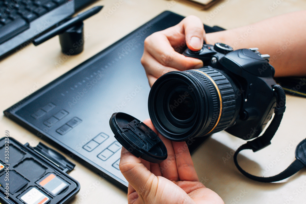 unrecognizable person holding a camera and removes the lens cap in his workplace unrecognizable person holding a camera and removes the lens cap in his workplace
