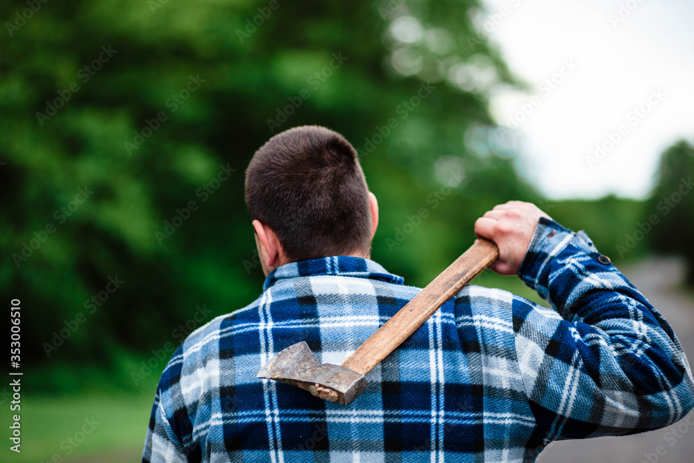 A lumberjack works in the forest. Lumberjack with an ax in the summer forest. The lumberjack is holding an ax. The lumberjack holds an ax on his back. The lumberjack shows the class. Ax in hand. A lumberjack works in the forest. Lumberjack with an ax in the summer forest. The lumberjack is holding an ax. The lumberjack holds an ax on his back. The lumberjack shows the class. Ax in hand.