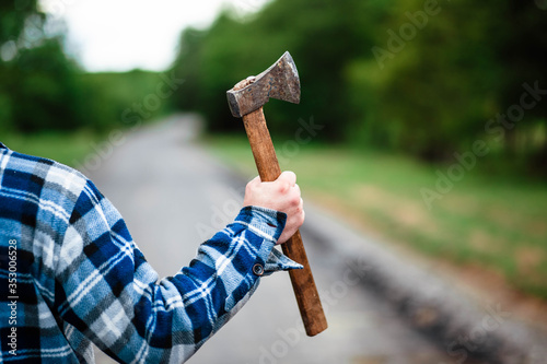 A lumberjack works in the forest. Lumberjack with an ax in the summer forest. The lumberjack is holding an ax. The lumberjack holds an ax on his back. The lumberjack shows the class. Ax in hand.