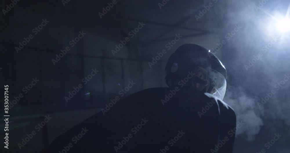 Camera round shot of Caucasian handsome male hockey player in uniform and helmet getting ready to hit on icy arena during game. Concentrated sportsman at match on ice in darkness.