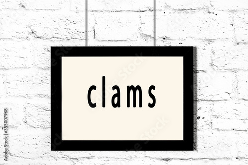 Black frame hanging on white brick wall with inscription clams photo
