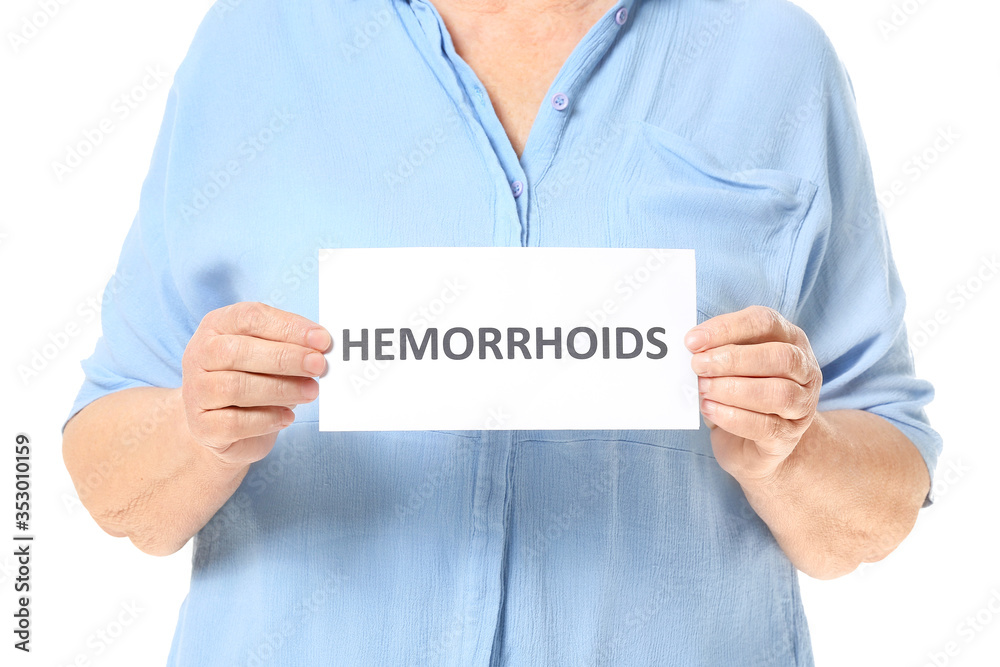 Elderly woman holding paper with text HEMORRHOIDS on white background Elderly woman holding paper with text HEMORRHOIDS on white background