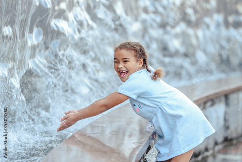 Happy beautiful girl running through the spray of water.