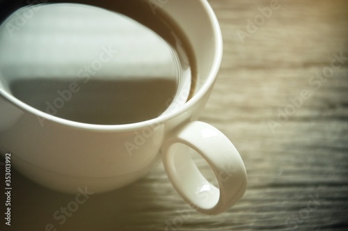 A coffee cup on the wooden textured  Blurred  white coffee mug with Reflection from sun light in a cup black coffee