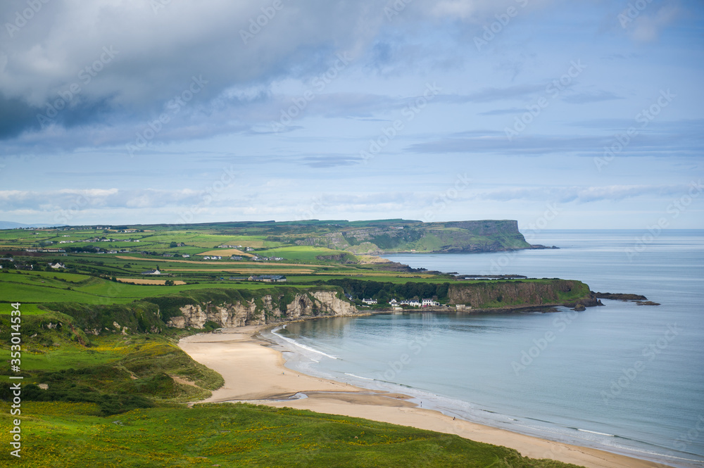 Costal view near Ballitoy, County Atrim, Northern Ireland. Beautiful green landscape with cliffs and sandy beaches. Some buildings are visible.