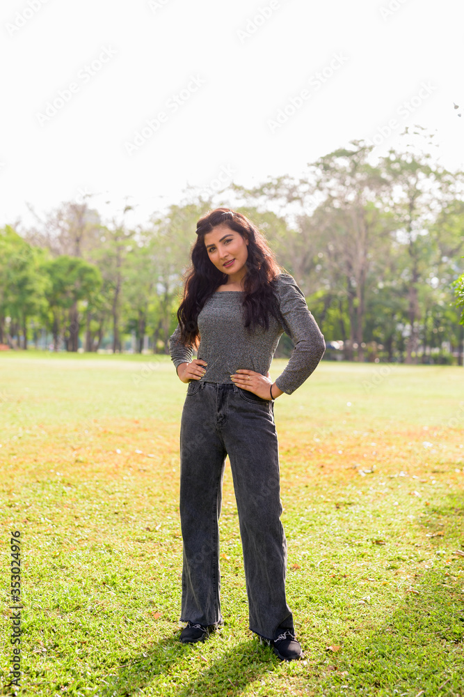 Full body shot of happy young beautiful Indian woman smiling at the park outdoors Full body shot of happy young beautiful Indian woman smiling at the park outdoors