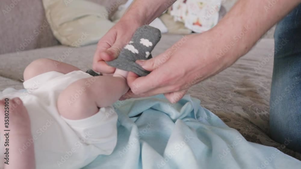 Dad puts a sock on the foot of a newborn. newborn baby lies on bed close up Dad puts a sock on the foot of a newborn. newborn baby lies on bed close up