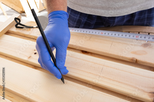 Closeup shot of assembling furniture. Man using measuring tape and pen and marking wooden desk for drilling or saw cut. Carpentry work concept