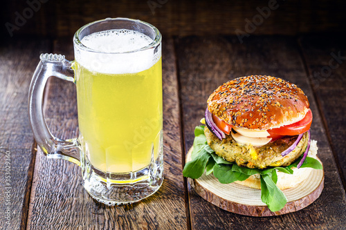 tasty vegetarian burger, homemade on wooden table with fresh vegetables around and mug of beer in the background, gourmet burger