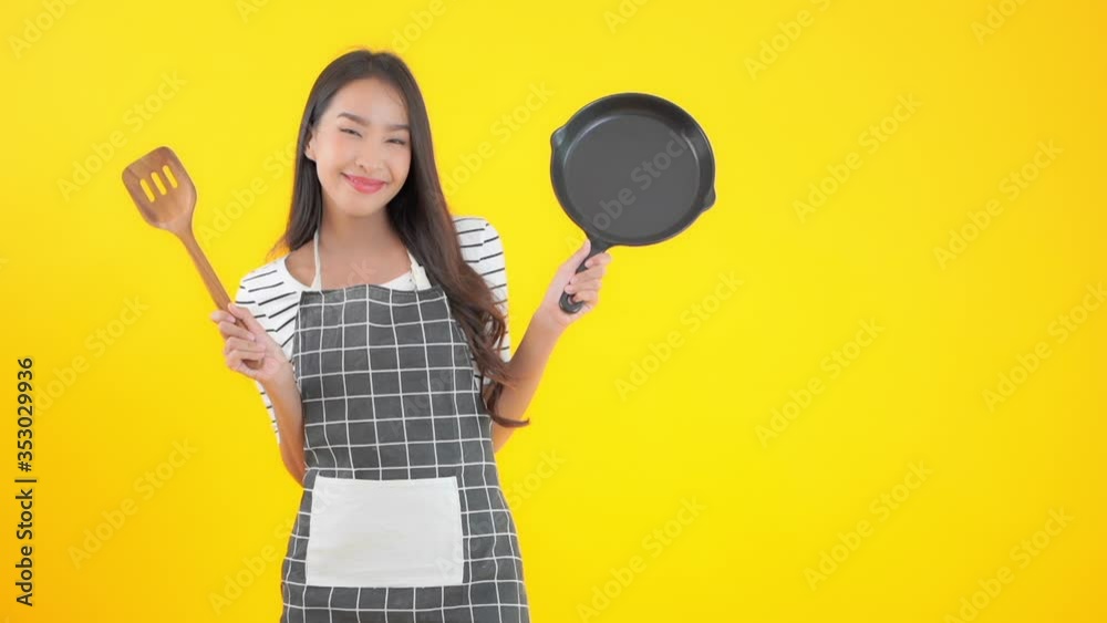 Attractive Asian Female Preparing For Cooking and Showing Dripping Pan and Mixing Spoon, Isolated on Yellow Background Attractive Asian Female Preparing For Cooking and Showing Dripping Pan and Mixing Spoon, Isolated on Yellow Background