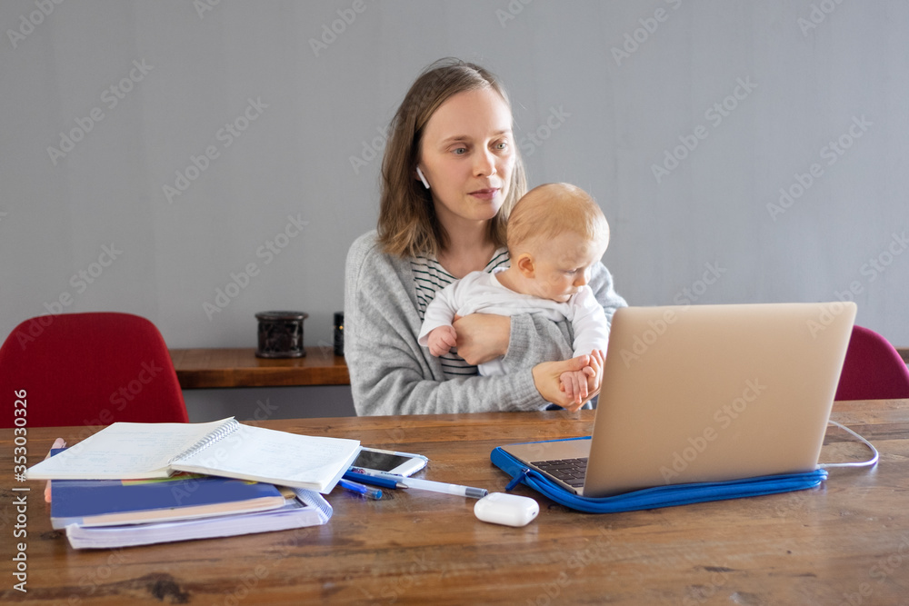 Mother working at home during quarantine. Young woman holding cute baby girl and looking at computer screen. Online connection and staying at home concept Mother working at home during quarantine. Young woman holding cute baby girl and looking at computer screen. Online connection and staying at home concept