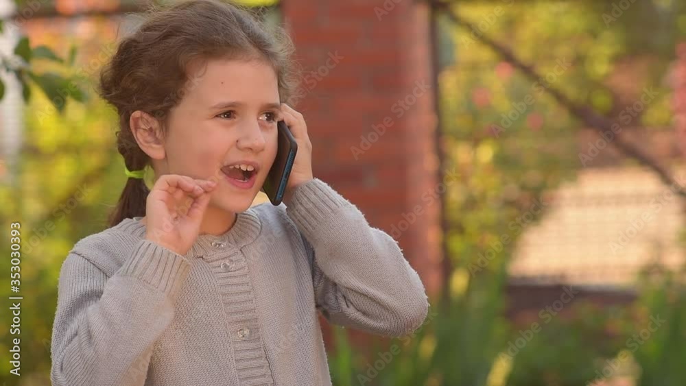 the girl is talking on the phone and smiling, the child tells the good news through mobile communication the girl is talking on the phone and smiling, the child tells the good news through mobile communication