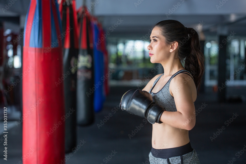 Portrait of a confident young athlete woman posing in boxing gloves at boxing gym background