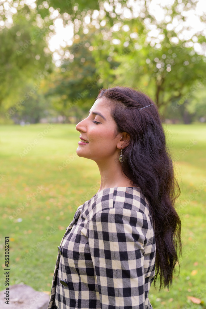 Profile view of happy young beautiful Indian woman smiling with eyes closed at the park outdoors
