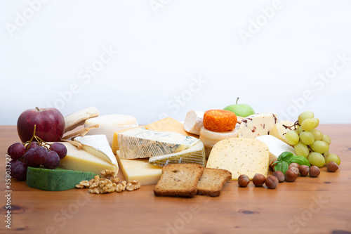 Different cheeses set, bread, whole apples, bunches of grapes and nuts on brown wooden table. Closeup, copy space. Gourmet and delicious snacks concept