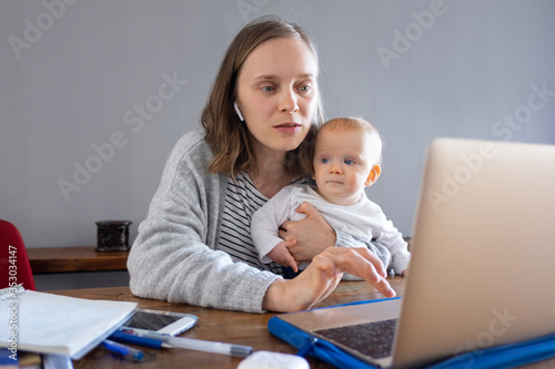Mother holding daughter and calling to family via laptop. Woman with red-haired baby girl looking at computer screen. Online connection and video call worldwide at home concept © Mangostar