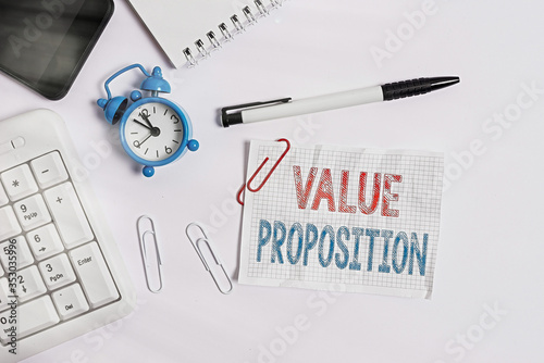 Conceptual hand writing showing Value Proposition. Concept meaning feature intended to make a company or product attractive Flat lay above computer mobile phone clock pencil and note paper photo