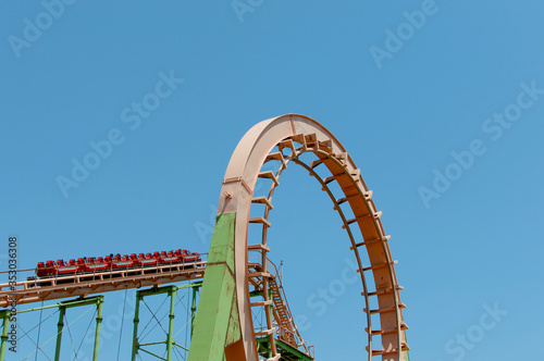 A loop of a scary roller coaster on blue sky background with copy space. A red cart rides on a switchback